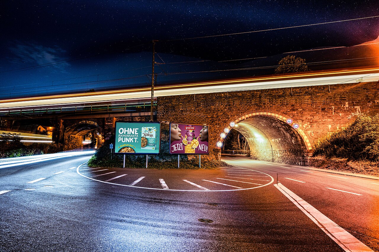 Zwei Großplakate an einer Straßenunterführung bei Nacht.