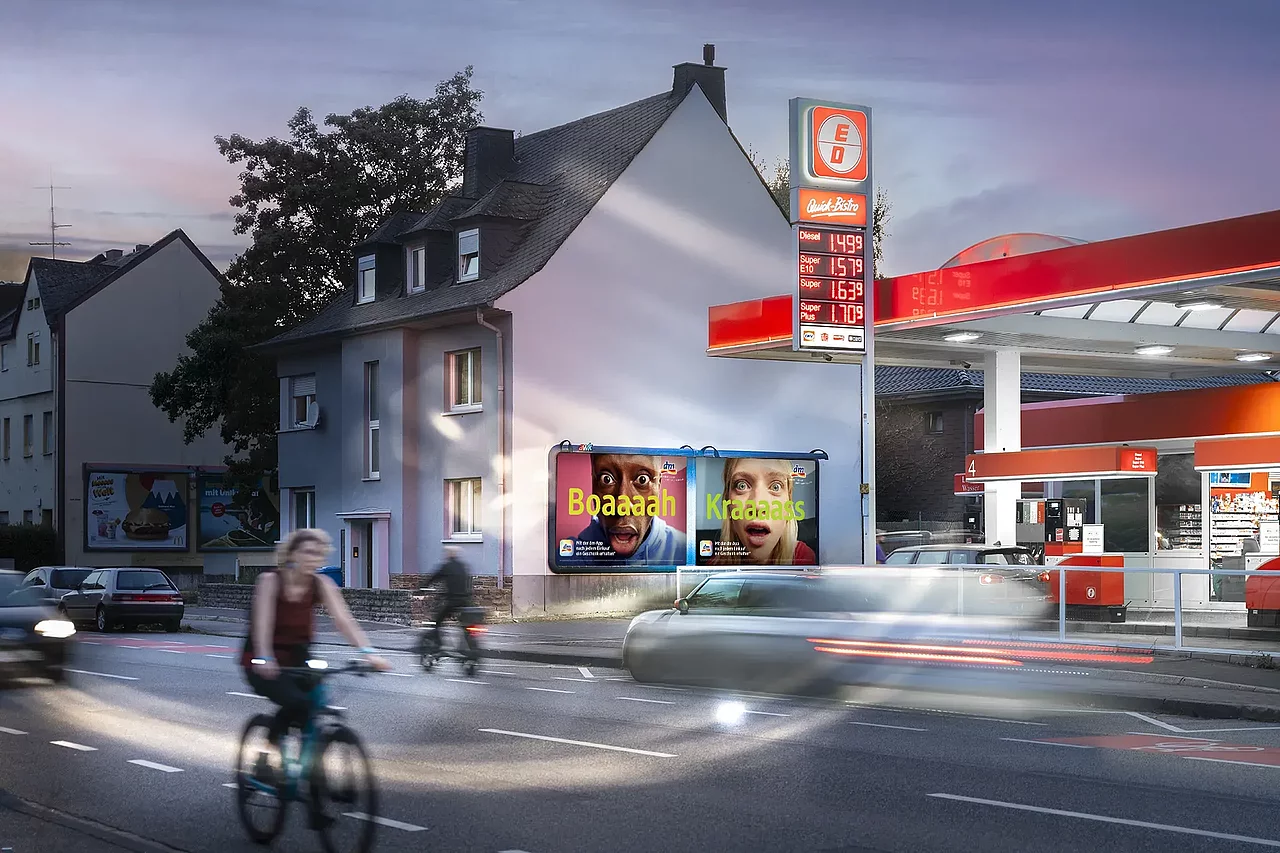 Werbeplakat mit den Slogans 'Boaah' und 'Kraass' und zwei Gesichtern. Das Plakat ist an einer gut sichtbaren Straßenecke platziert und zieht die Aufmerksamkeit von Autofahrern und Passanten an.