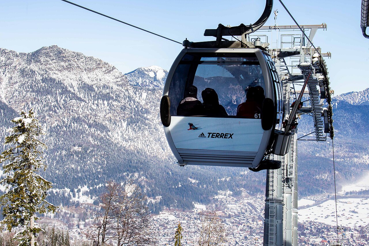 Seilbahn im Gebirge mit Werbung für adidas Terrex auf der Seite der Gondel. Die Aussicht auf die schneebedeckten Berge ergänzt das Abenteuergefühl.
