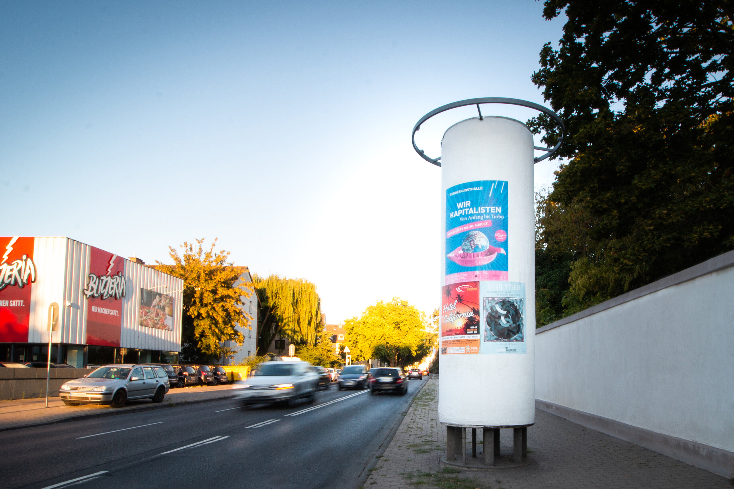 Plakatsäule an einer Straße mit drei verschiedenen Plakaten