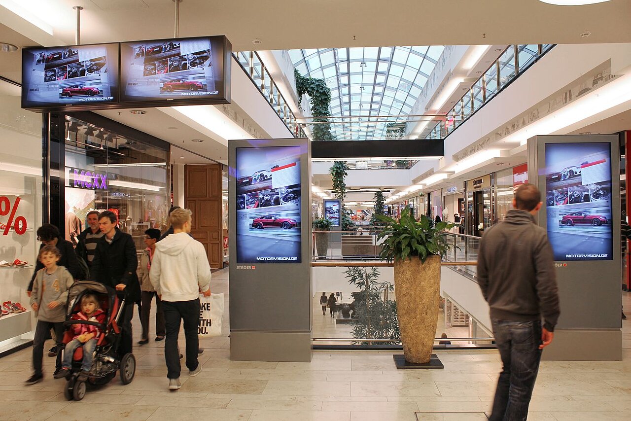 Digitale Werbescreens mit Automotiv in einem Einkaufszentrum, ideal für aufmerksamkeitsstarke Außenwerbung mit hoher Besucherfrequenz.